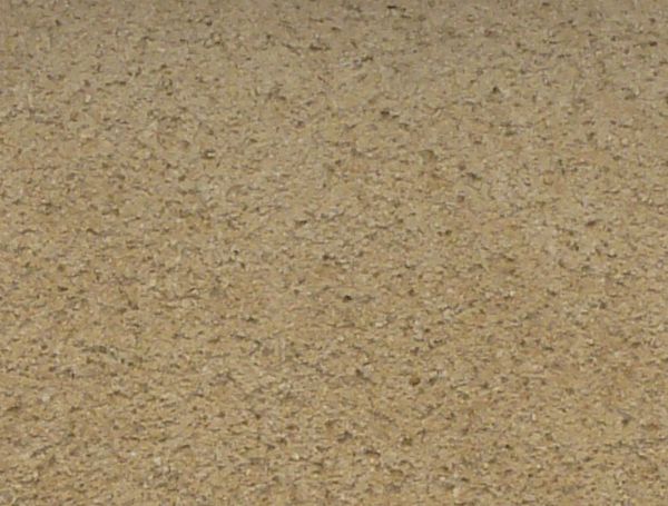 Concrete fence texture made up of a solid tan wall with a coarse, fine texture, similar columns with white trim on either side, and a dark brown tile awning along the top. Discoloration is visible near the bottom of the wall.